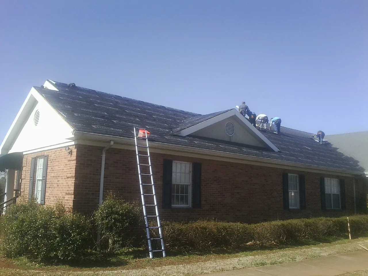Crew tearing shingles off a brick ranch roof with a ladder set — Emergency Roof Repair work by our crew in Mount Joy