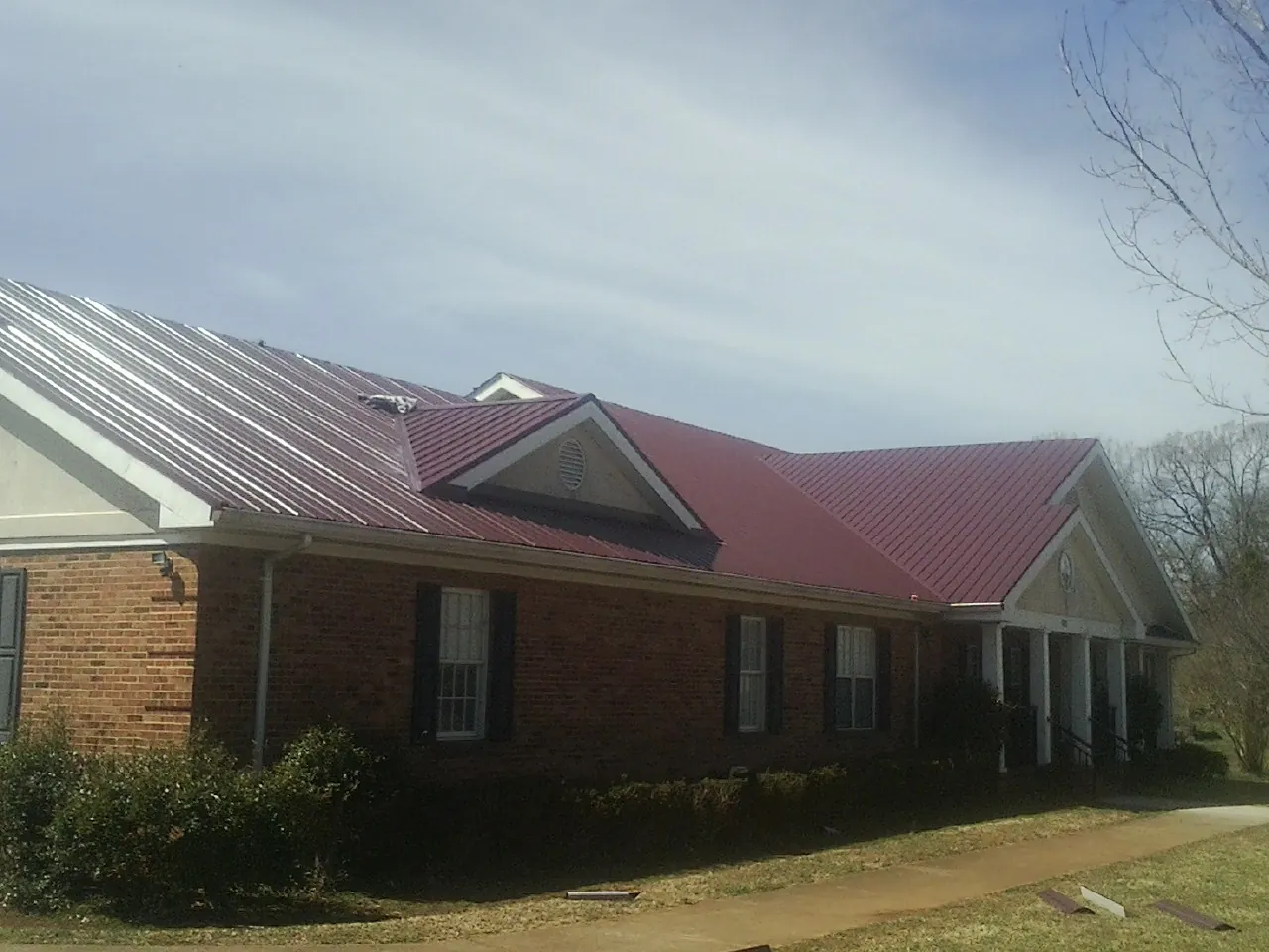 Red metal roof with gabled entries on a long brick building, from a Hail Damage Roof Repair job in Mount Joy