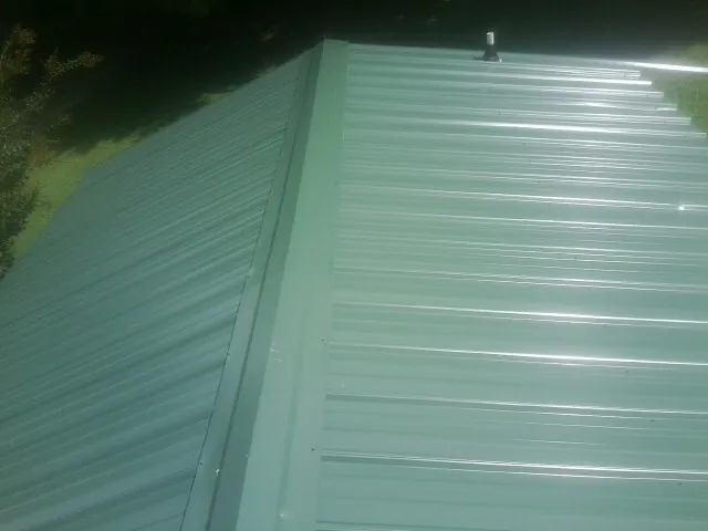 New green metal panels meeting at the ridge of a roof — Flat Roof Repair work by our crew in Mount Joy