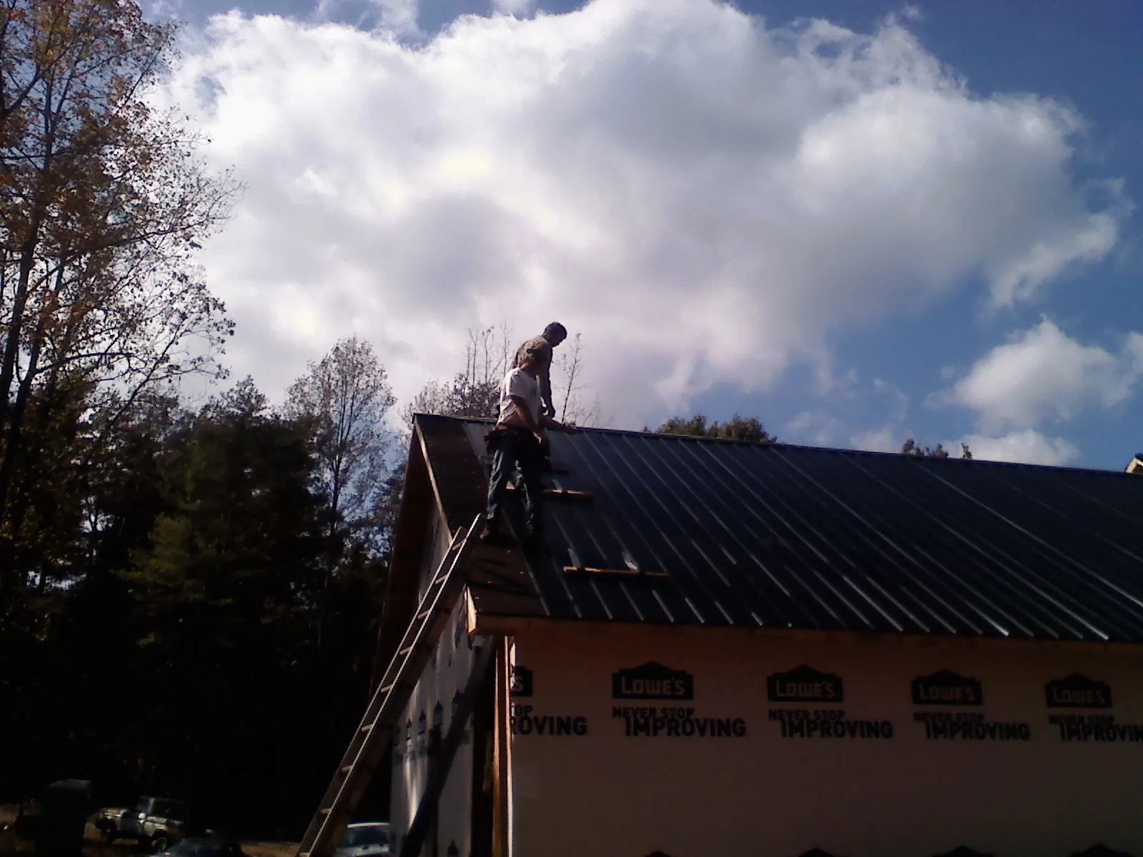 Roofer fastening dark metal panels high against a cloudy sky, from a Roof Inspection job in Mount Joy