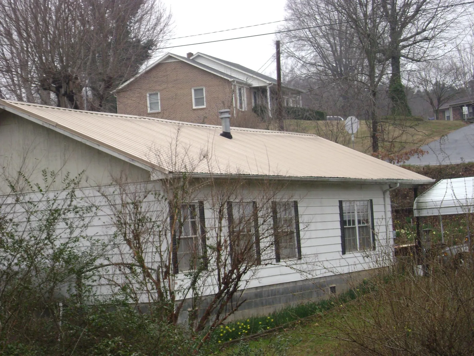 Tan metal roof on a white sided house set into a hillside — Commercial Roofing by Roofing Brothers in Mount Joy